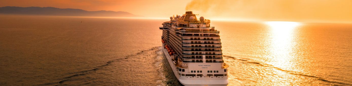 Oceanwide Expeditions: Ein großes, weißes Kreuzfahrtschiff gleitet auf dem Meer dem Sonnenuntergang entgegen