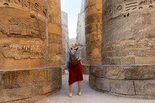 Frühbucher: Eine Frau mit Sonennhut steht zwischen riesigen Säulen mit Hyroglyphen