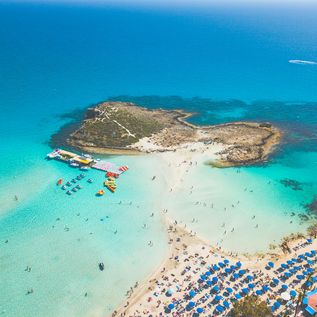 Nahe einem vollen Strand am türkis-blauem Meer, befindet sich eine Insel.