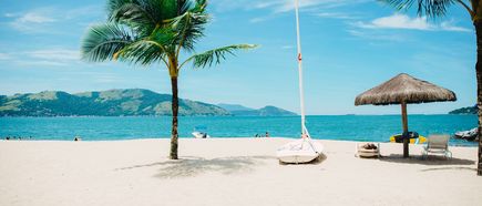 Ein weißer Strand mit Palme, Sonnenschirm und Booten.