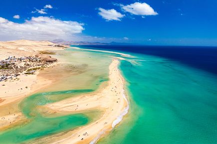 Kanaren Urlaub: Eine Luftaufnahme eines goldenen, breiten Sandstrands der in eine Wüstenlandschaft übergeht direkt am türkisen Meer.
