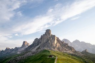 Italien Urlaub: Eine imposante, graue Berglandschaft und eine Hütte auf einem grünen berg.
