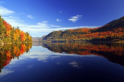 Ein blauer, spiegelglatter See an herbstlich, bunten Wäldern