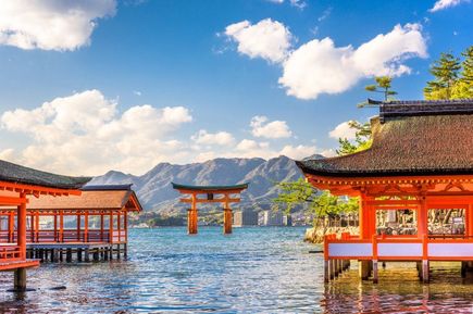 Rote, asiatische Tempel stehen auf einem klaren See. Im Hintergrund Berge.