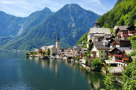Urlaub mit Kindern: Ein idyllisches Dorf mit Kirche in einer Berglandschaft grenzt an einen spiegelglatten Berg