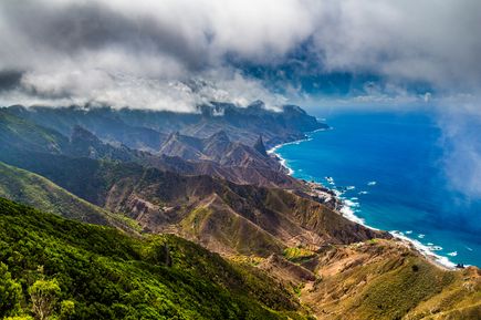 Kanaren Urlaub: Eine Luftaufnahme einer grünen, steilen Berglandschaft am tiefblauen Meer.