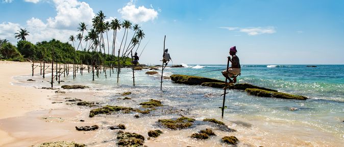 Fischer sitzen auf Holzstäben am Ufer eines Strands auf Sri Lanka