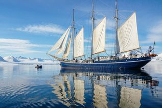 Oceanwide Expeditions: SV Rembrandt van Rijn auf dem spiegelglatten Wasser im Hintergrund Eisberge