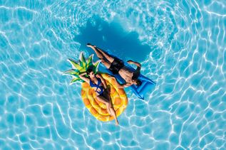 Ein junges Paar liegt auf Luftmatratzen im Pool