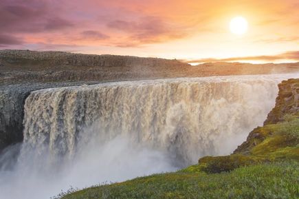 Ein gigantischer Wasserfall unter untergehender Sonne in orange-lilafarbenem Himmel.
