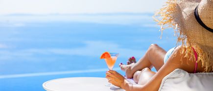 Eine Frau im Sonnenhut und Cocktail liegt entspannt auf einer Sonnenliege und blickt aufs Meer. All inclusive Urlaub.