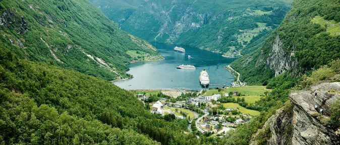 Kreuzfahrten: weiße, riesige Kreuzfahrtschiffe fahren durch einen grünen, norwegischen Fjord