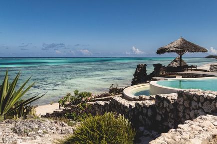 Eine Poollandschaft eines Hotels grenzt direkt an einen tropischen Strand.