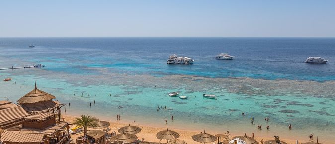 Osterurlaub: EIn Sandstrand mit Sonnenliegen- und schirmen am türkis blauen Riff