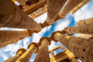 Riesige Säulen mit ägyptischen Hieroglyphen ragen in den blauen Himmel.