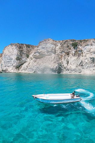 Kreta: Ein weißes, leeres Motorboot auf glasklarem, türkisem Wasser, im Hintergrund ein Felsen