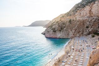 Ein belebter Sandstrand mit vielen Sonnenliegen zwischen Felsen