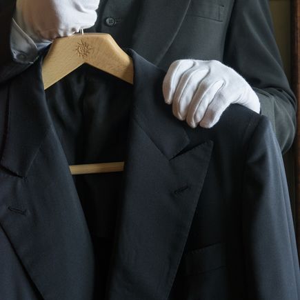 MSC Yacht Club: Ein Butler im schwarzen Anzug und weißen Handschuhen hält einen schwarzen Blazer mit MSC Bügel in den Händen.