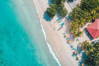 Strandurlaub: Luftaufnahme von einem weißen Sandstrand am türkis-blauen Meer
