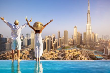 Städtereisen: Ein Paar mit Sonnenhüten steht am Rand eines Infinitypools mit Blick auf die Skyline von Dubai