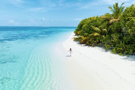 Eine Frau läuft an einem einsamen weißen Strand auf den Malediven