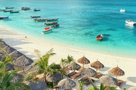 Kreuzfahrten 2026: Ein Sandstrand mit Sonnenschirmen und Liegen am türkisen Meer mit Booten
