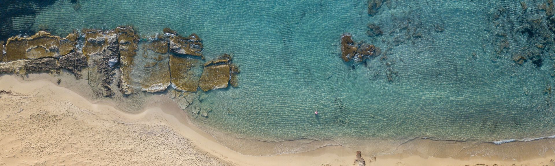 Kreta: Eine Luftaufnahme eines Sandstrands mit ein paar Felsen mit türkisem, glasklarem Wasser