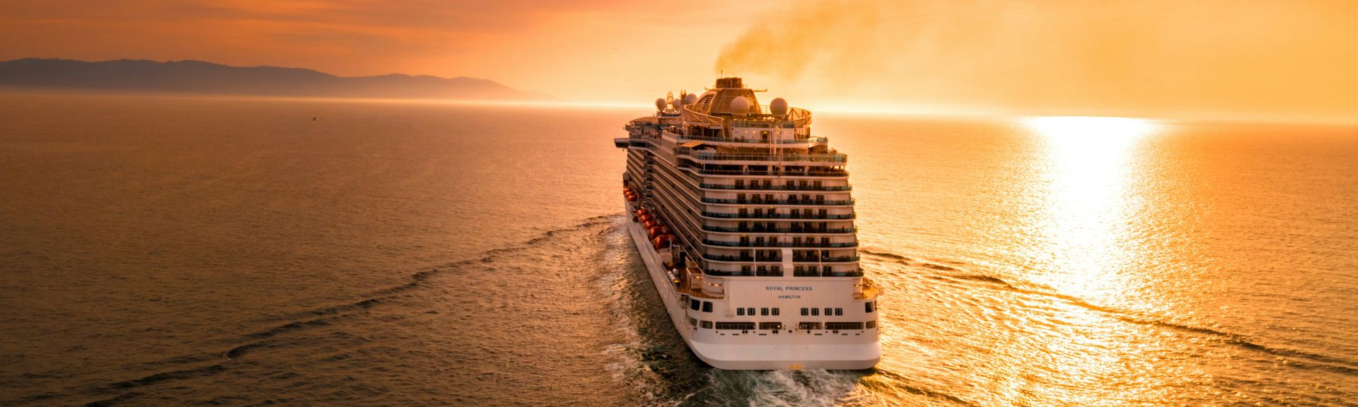 Kreuzfahrten 2026: Ein großes, weißes Kreuzfahrtschiff gleitet auf dem Meer dem Sonnenuntergang entgegen