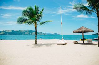 Ein weißer Strand mit Palme, Sonnenschirm und Booten.