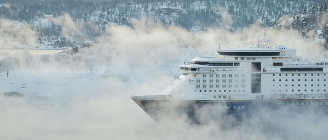 Kreuzfahrten: Ein weißes Kreuzfahrtschiff, fährt durch eine winterliche, verschneite, nebelige Landschaft