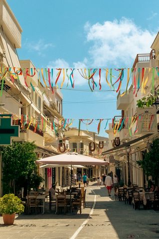 Kreta: Eine Straße mit Außengastronomie und bunten Girlanden von links nach rechts gespannt
