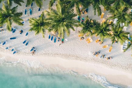 Eine Luftaufnahme eines weißen Strands am türkisen Wasser mit tropischen Palmen
