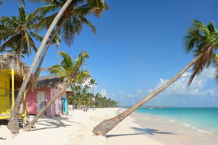 Kreuzfahrten 2026: Ein weißer Strand mit Palmen und bunten Holzhäusern