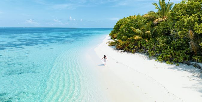Adults only: Eine Frau läuft an einem einsamen weißen Strand entlang