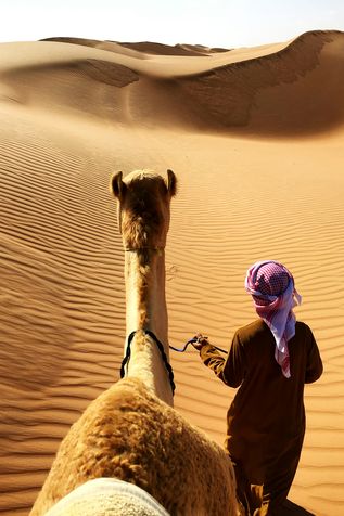 Urlaub im Orient: Ein traditionell, arabisch gekleideter Mann führt ein Kamel durch die Wüste 