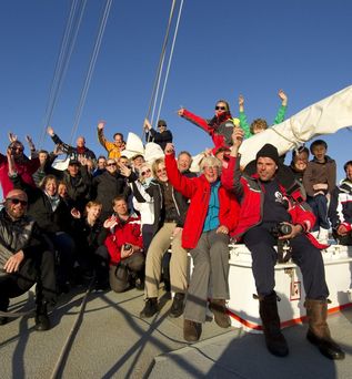 Oceanwide Expeditions: Eine Gruppe von ca. 20 Menschen in Outdoor-Kleidung hebt die Hände in die Luft auf einem Segelschiff