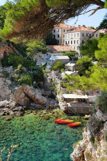 Kroatien Urlaub: Blick auf eine verstecke Bucht mit vielen Felsen, am Ufer drei bunte Boote und drei Standup Paddles