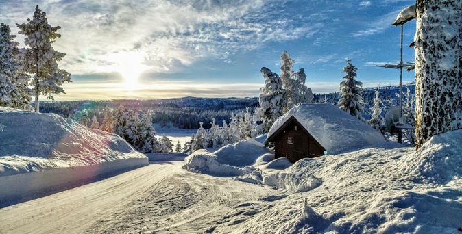 Winterurlaub in den Bergen: Eine verschneite Berg- und Landschaft unter blauem Himmel mit einer braunen schneebedeckten Hütte.