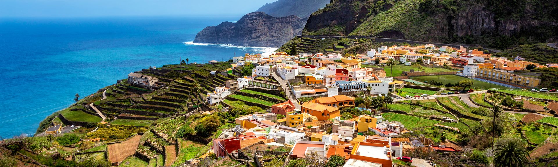 Kanaren Urlaub: Eine Luftaufnahme von grünen Bergen, mit mediterranen Häusern direkt am Meer