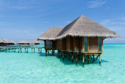 Malediven Urlaub: im türkisen, glasklaren Wasser stehen Holzbungalows auf Stelzen im Wasser
