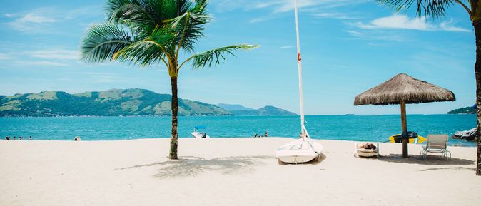 Ein weißer Strand mit Palme, Sonnenschirm und Booten.