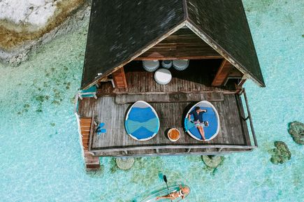 Luxus: Eine Luftaufnahme eines Holzbungalows auf türkisem, glasklaren Wasser