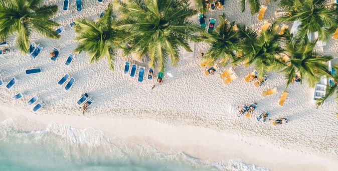 Eine Luftaufnahme eines weißen Strands am türkisen Wasser mit tropischen Palmen